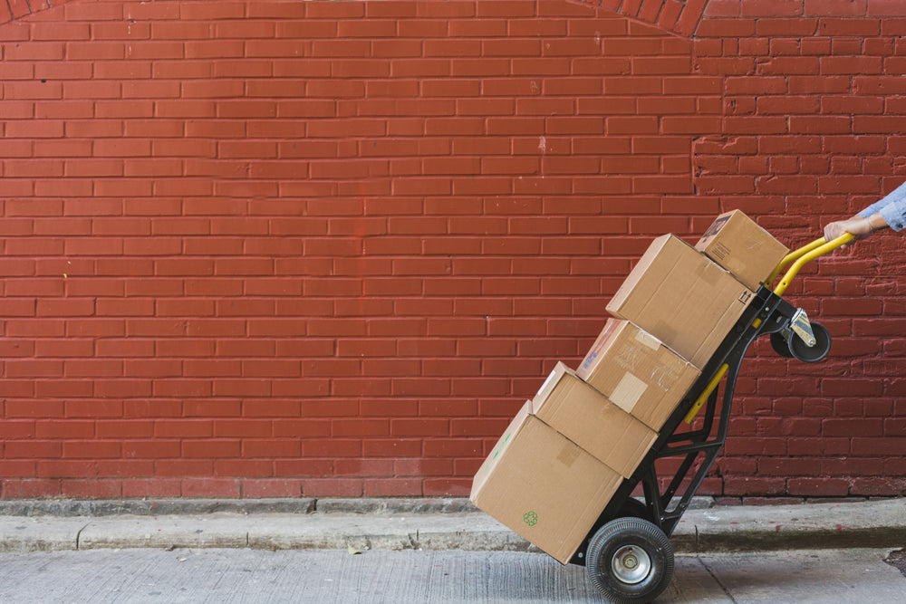 A person pushing several boxes on a dolly 